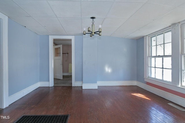 spare room with a drop ceiling, dark hardwood / wood-style flooring, and an inviting chandelier