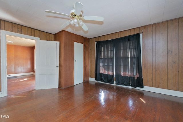 unfurnished room with ceiling fan, dark wood-type flooring, and wooden walls