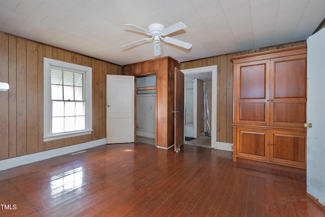 unfurnished bedroom with ceiling fan, a closet, dark wood-type flooring, and wood walls