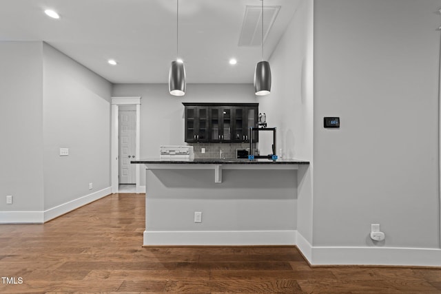 kitchen featuring a breakfast bar, dark hardwood / wood-style flooring, kitchen peninsula, pendant lighting, and backsplash