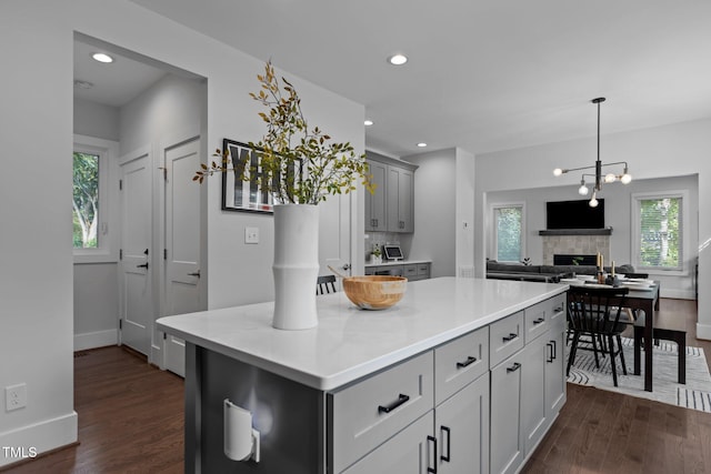 kitchen featuring dark wood-type flooring, gray cabinetry, a fireplace, a center island, and decorative backsplash