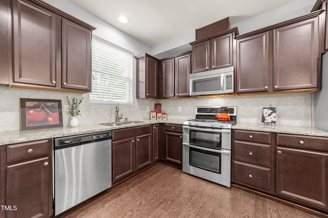 kitchen with appliances with stainless steel finishes, sink, dark brown cabinets, light stone countertops, and dark wood-type flooring