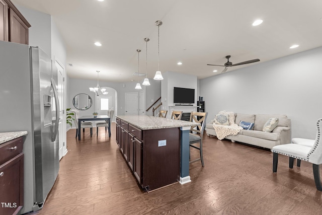 kitchen featuring a breakfast bar, a center island, light stone countertops, stainless steel fridge with ice dispenser, and decorative light fixtures