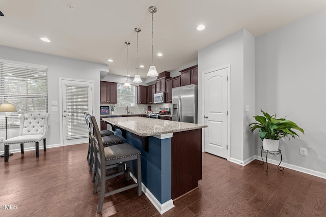 kitchen with dark brown cabinetry, a breakfast bar area, decorative light fixtures, a kitchen island, and stainless steel appliances