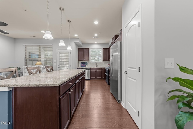 kitchen with a kitchen island, a breakfast bar, pendant lighting, appliances with stainless steel finishes, and dark hardwood / wood-style flooring