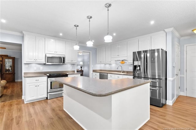 kitchen with pendant lighting, appliances with stainless steel finishes, a kitchen island, white cabinetry, and light hardwood / wood-style flooring