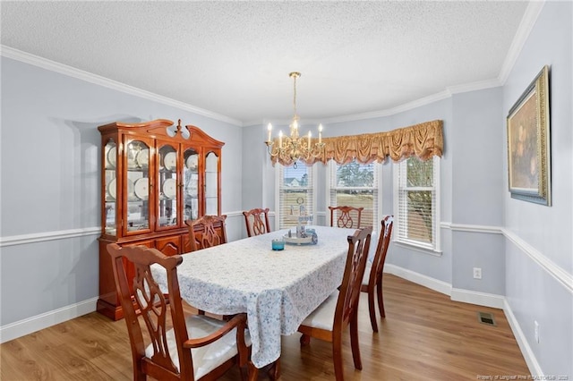 dining room featuring wood-type flooring, a textured ceiling, crown molding, and an inviting chandelier