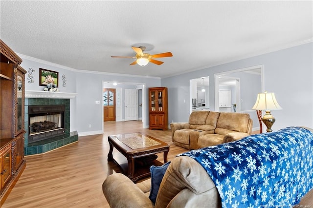 living room with hardwood / wood-style floors, a textured ceiling, ceiling fan, a tile fireplace, and crown molding