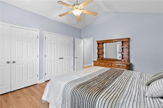 bedroom with vaulted ceiling, ceiling fan, two closets, and light hardwood / wood-style flooring