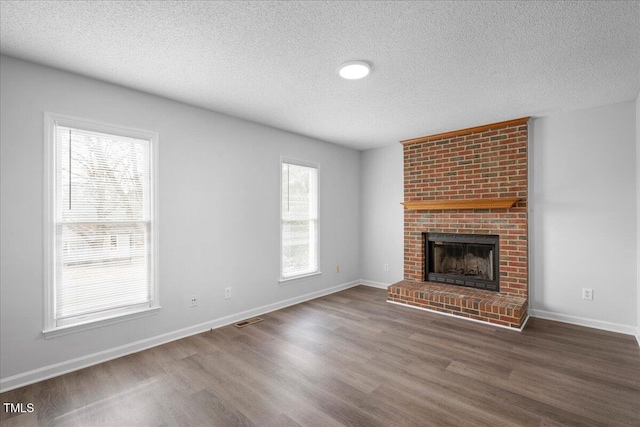 unfurnished living room featuring a brick fireplace, dark wood-type flooring, and a textured ceiling