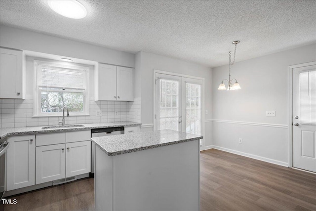 kitchen featuring sink, white cabinetry, light stone countertops, a kitchen island, and decorative light fixtures