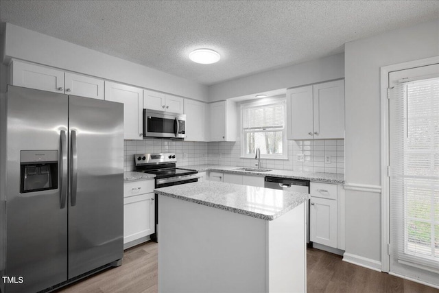 kitchen with appliances with stainless steel finishes, sink, white cabinets, a center island, and light stone countertops