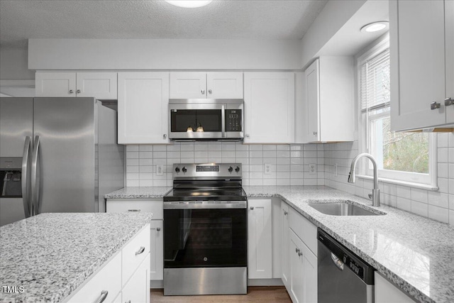 kitchen with sink, white cabinetry, appliances with stainless steel finishes, light stone countertops, and backsplash