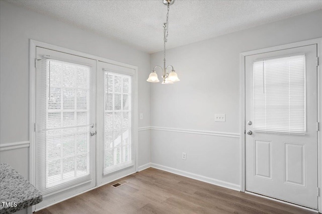 doorway to outside featuring hardwood / wood-style flooring, a chandelier, and a textured ceiling