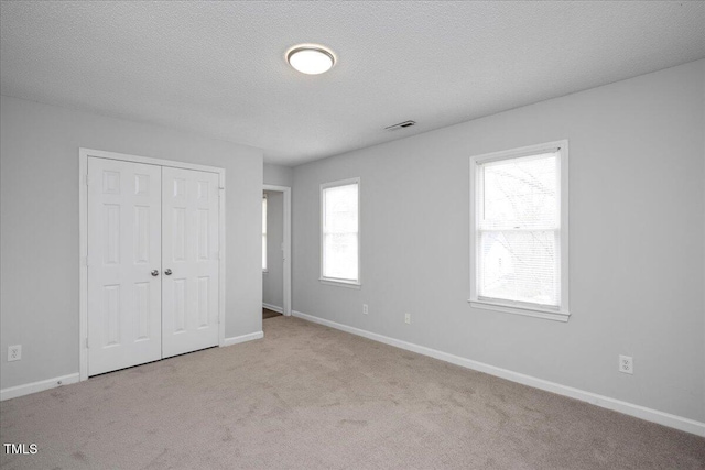 unfurnished bedroom featuring light carpet, a closet, and a textured ceiling