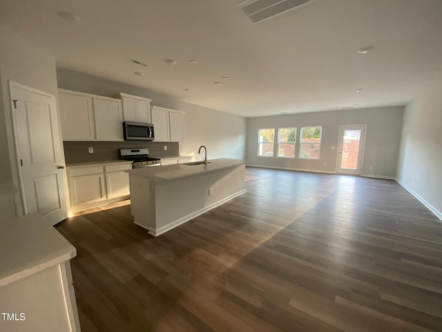 kitchen with appliances with stainless steel finishes, white cabinetry, dark hardwood / wood-style flooring, backsplash, and a center island with sink