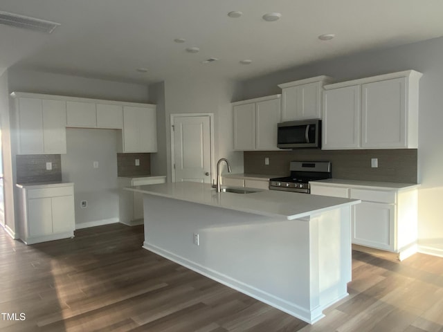 kitchen with white cabinets, appliances with stainless steel finishes, dark hardwood / wood-style floors, and an island with sink