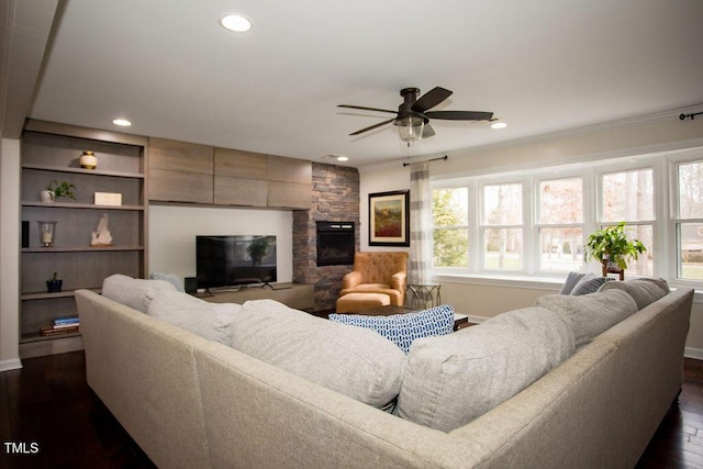 living room with dark hardwood / wood-style flooring, a stone fireplace, crown molding, and ceiling fan