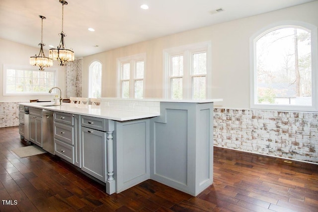 kitchen featuring gray cabinetry, pendant lighting, brick wall, and a center island with sink