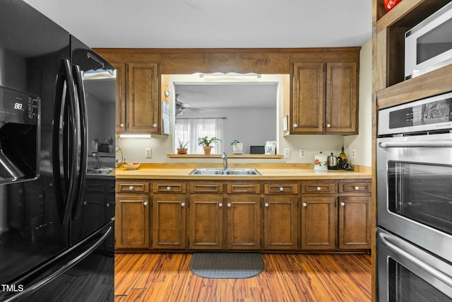 kitchen with double oven, sink, light wood-type flooring, and black fridge