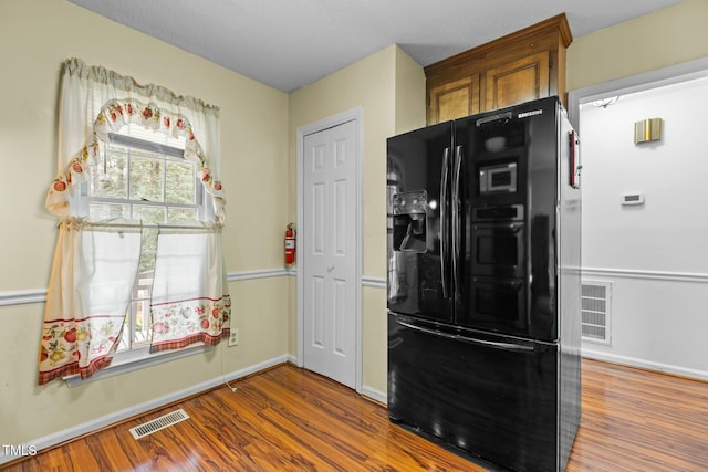 kitchen featuring hardwood / wood-style flooring and black refrigerator with ice dispenser