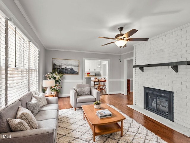 living room featuring crown molding, wood-type flooring, a fireplace, and ceiling fan