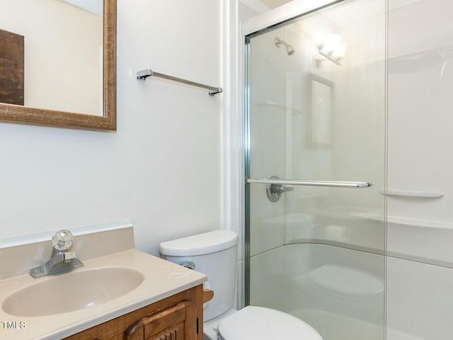 bathroom featuring a shower with door, vanity, and toilet