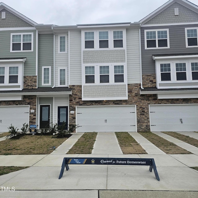 townhome / multi-family property with concrete driveway, stone siding, and an attached garage