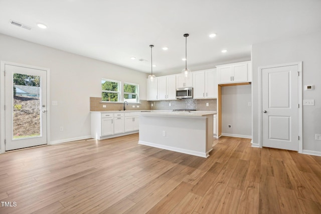 kitchen featuring pendant lighting, backsplash, white cabinetry, a kitchen island, and light hardwood / wood-style floors