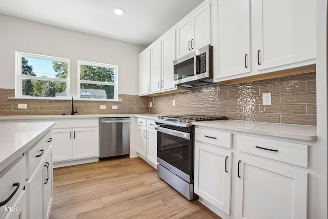 kitchen featuring light stone countertops, white cabinetry, stainless steel appliances, backsplash, and light wood-type flooring