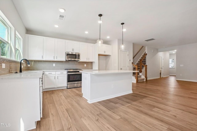 kitchen with a center island, appliances with stainless steel finishes, white cabinetry, sink, and decorative light fixtures