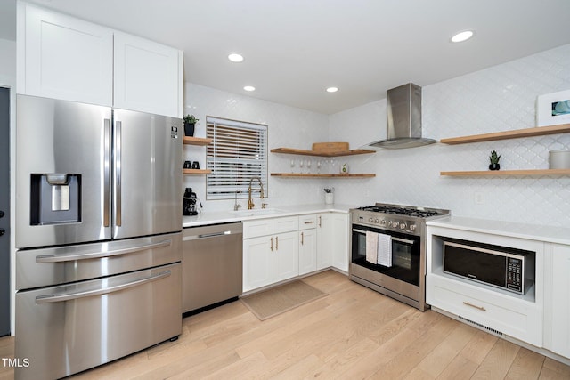 kitchen with sink, white cabinetry, light hardwood / wood-style flooring, stainless steel appliances, and wall chimney range hood