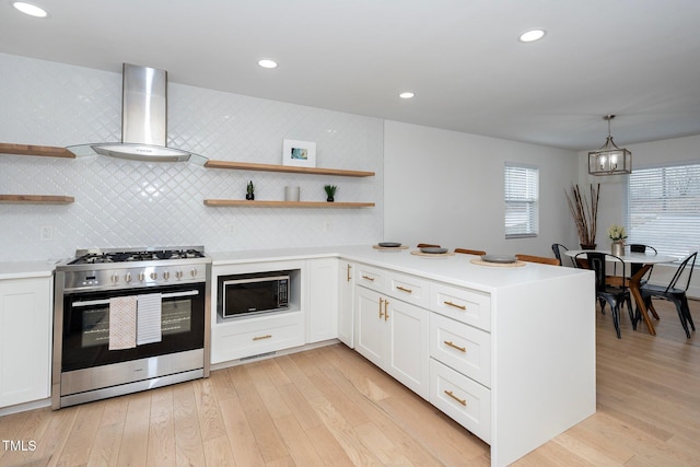 kitchen featuring stainless steel range with gas cooktop, built in microwave, white cabinets, hanging light fixtures, and wall chimney exhaust hood