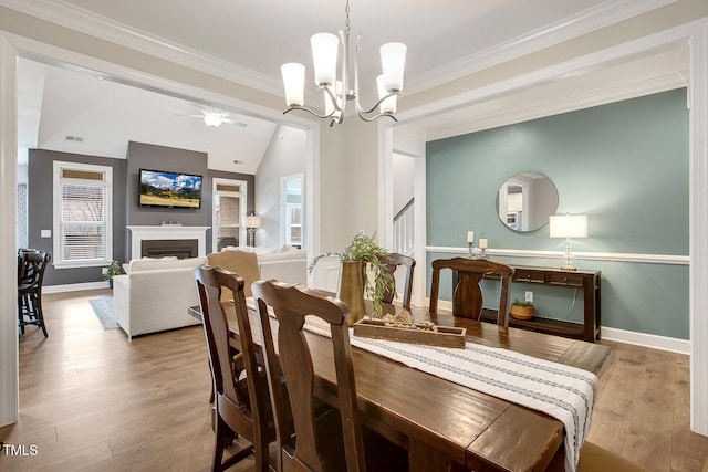 dining space featuring lofted ceiling, light hardwood / wood-style flooring, ornamental molding, a healthy amount of sunlight, and ceiling fan with notable chandelier