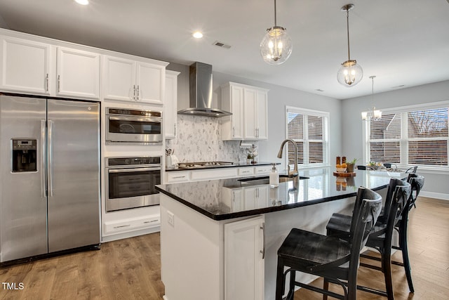 kitchen featuring stainless steel appliances, sink, a center island with sink, and wall chimney range hood