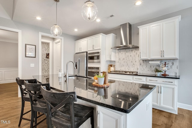 kitchen featuring pendant lighting, white cabinetry, stainless steel appliances, an island with sink, and wall chimney exhaust hood