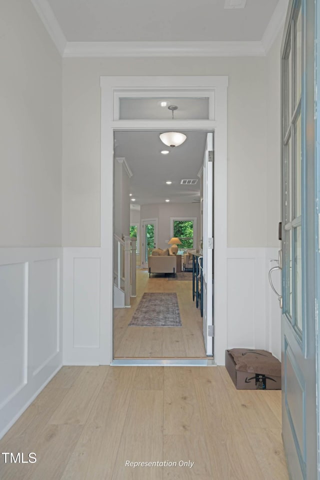 foyer entrance featuring light wood finished floors, visible vents, a decorative wall, and crown molding