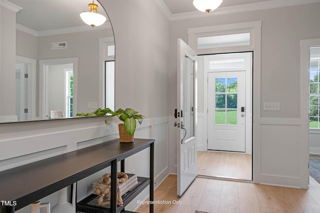 foyer with light wood finished floors, visible vents, and crown molding