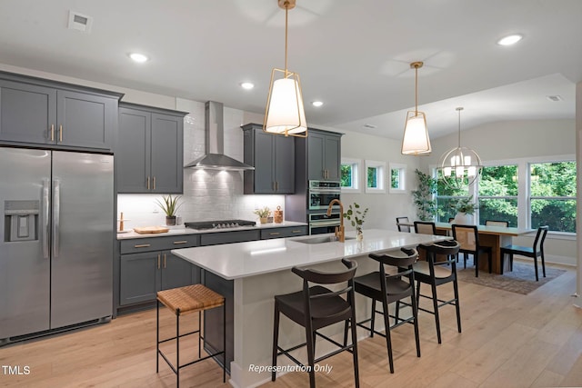 kitchen with lofted ceiling, wall chimney range hood, a kitchen bar, a kitchen island with sink, and stainless steel appliances