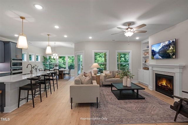 living room featuring ceiling fan, built in shelves, recessed lighting, light wood-type flooring, and a glass covered fireplace