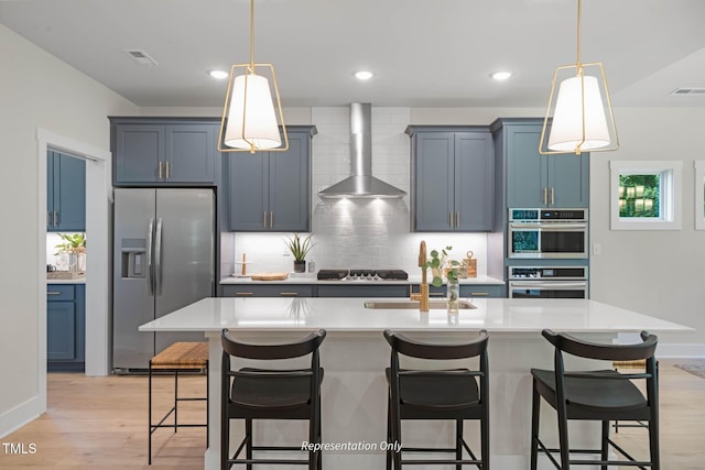 kitchen with a kitchen breakfast bar, stainless steel appliances, wall chimney exhaust hood, and an island with sink