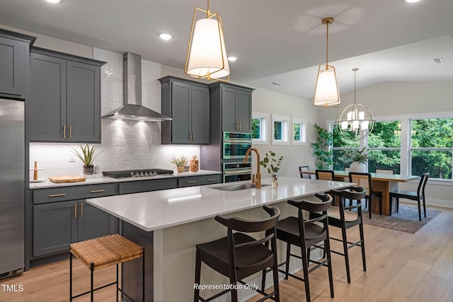 kitchen with a center island with sink, a breakfast bar area, stainless steel appliances, wall chimney range hood, and pendant lighting