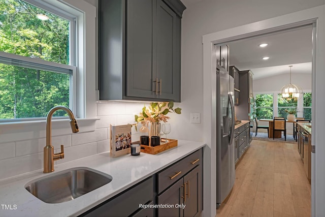 kitchen featuring stainless steel fridge with ice dispenser, decorative light fixtures, light stone countertops, vaulted ceiling, and a sink