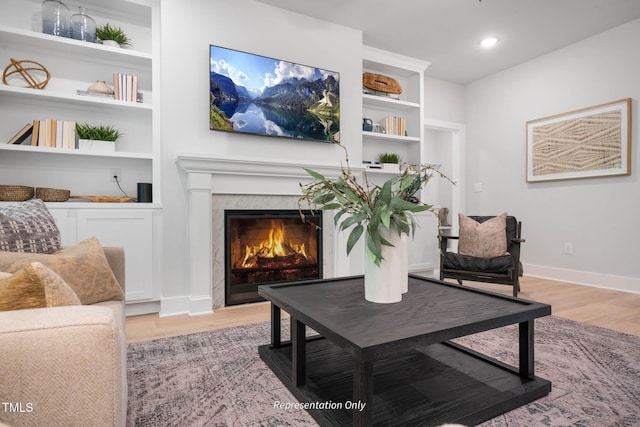 living area featuring a premium fireplace, light hardwood / wood-style floors, and built in shelves