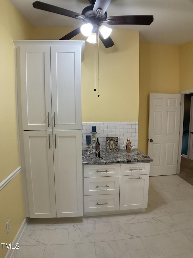 bar with decorative backsplash, white cabinets, and dark stone countertops