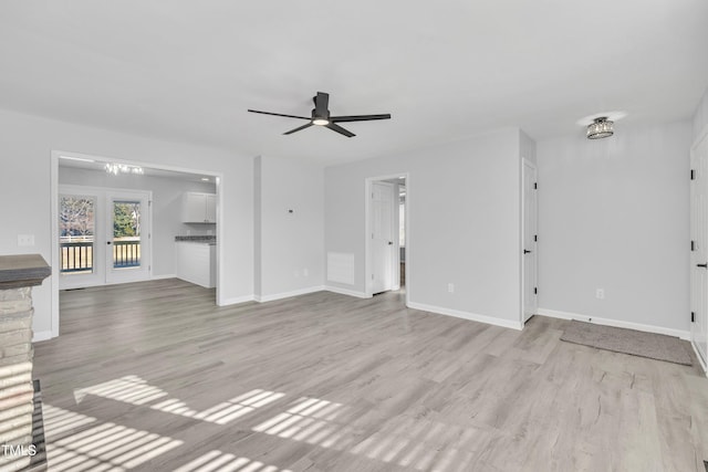 unfurnished living room featuring ceiling fan with notable chandelier and light hardwood / wood-style flooring