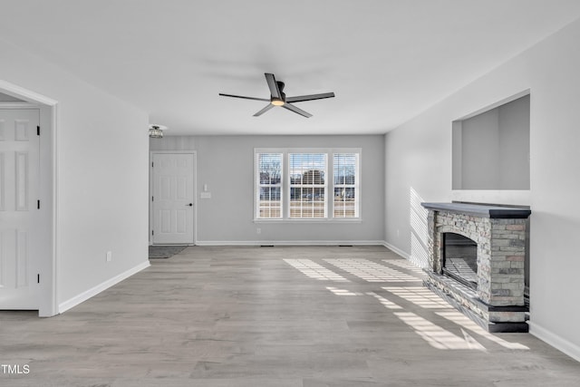 unfurnished living room featuring ceiling fan, a stone fireplace, and light wood-type flooring