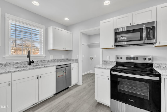 kitchen featuring light stone countertops, white cabinets, appliances with stainless steel finishes, sink, and light wood-type flooring