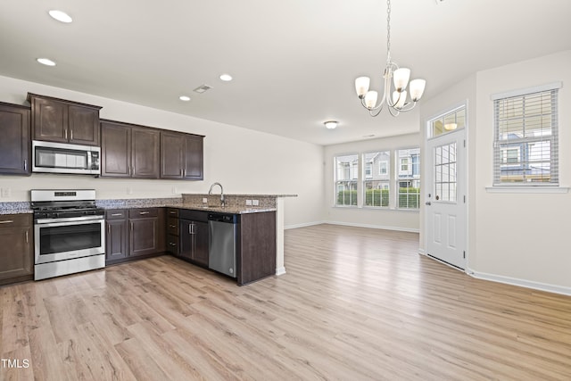 kitchen with appliances with stainless steel finishes, pendant lighting, light hardwood / wood-style floors, and kitchen peninsula