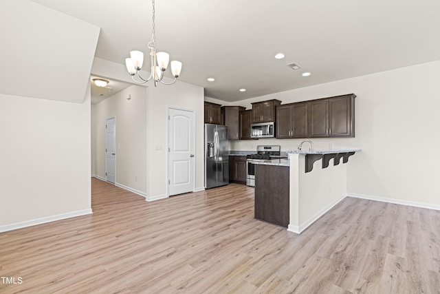 kitchen with a kitchen bar, appliances with stainless steel finishes, decorative light fixtures, light wood-type flooring, and dark brown cabinetry